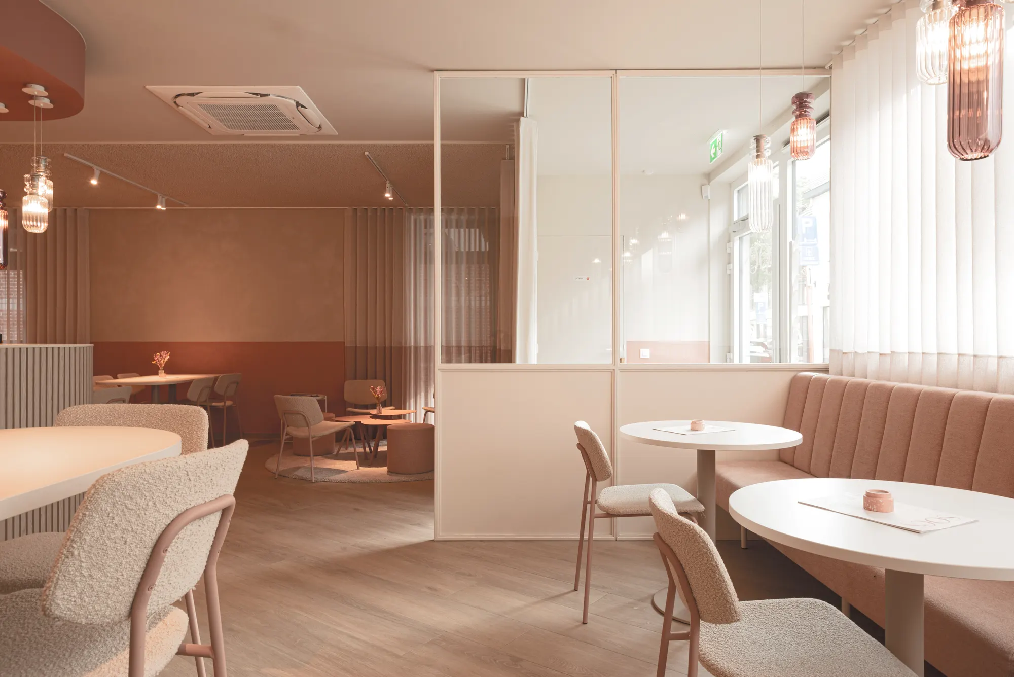 Het interieur van Soes in zachte roze tinten, met ronde tafels en een zitbank